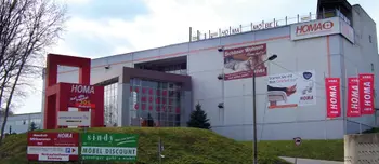 HOMA Gebäude mit Werbeschildern, Fahnen, Eingang und grünem Hang im Vordergrund